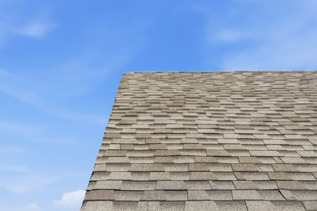 Completed architectural shingle roof ridge against a clear blue sky